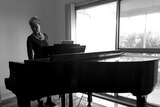 Former pianist Claire Cooper stands at her grand piano in her Brunswick home