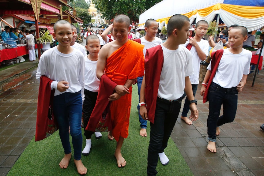 The boys walk with their former coach dressed in an orange monks' robe.