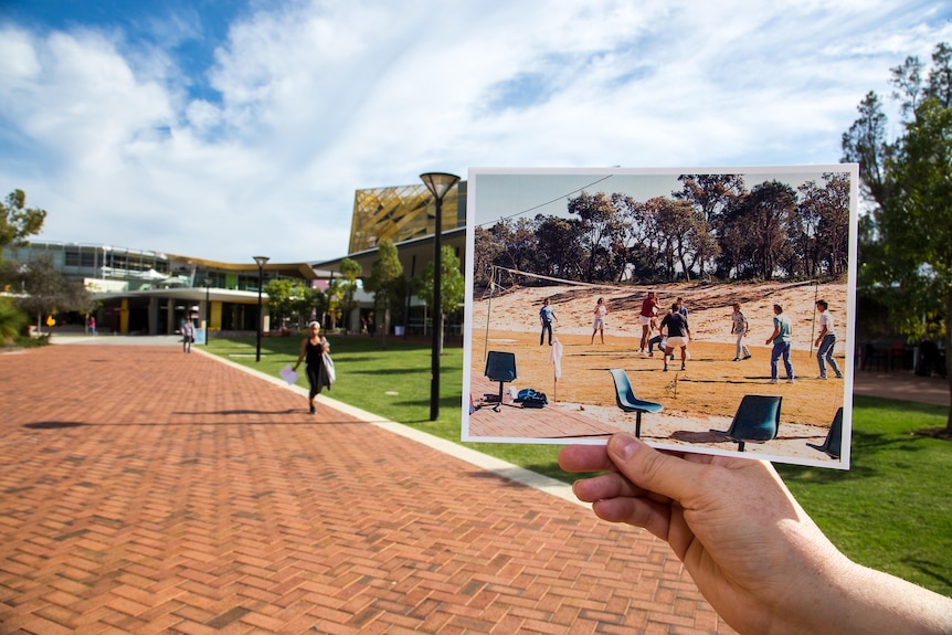 A hand holds up a photo of a uni campus in front of an actual shot of ho it looks today.