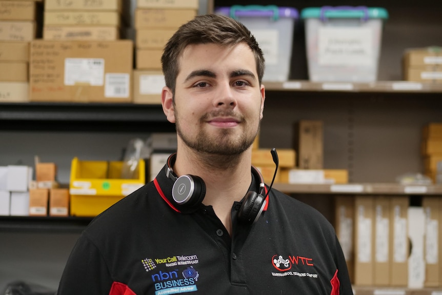 Young man wearing headphones with boxes of electronics behind