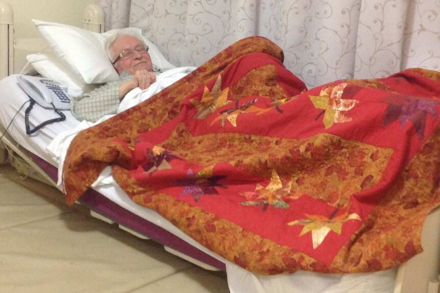 elderly man sleeping in bed with a phone next to him