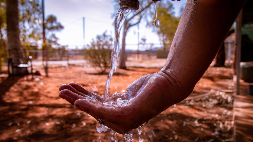 Water pours out of a tap  into someone's hand in a desert community.