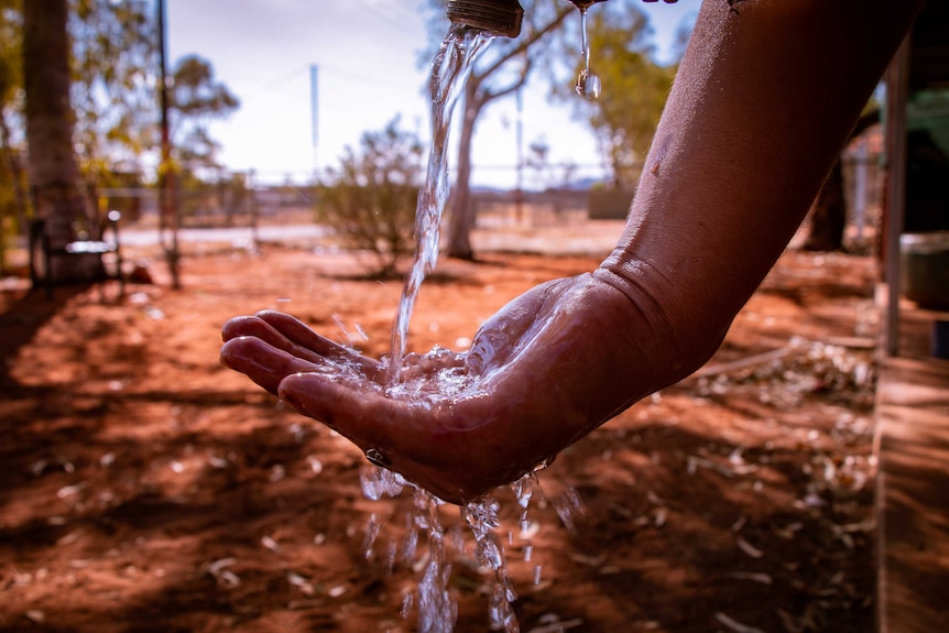 Water pours out of a tap  into someone's hand in a desert community.