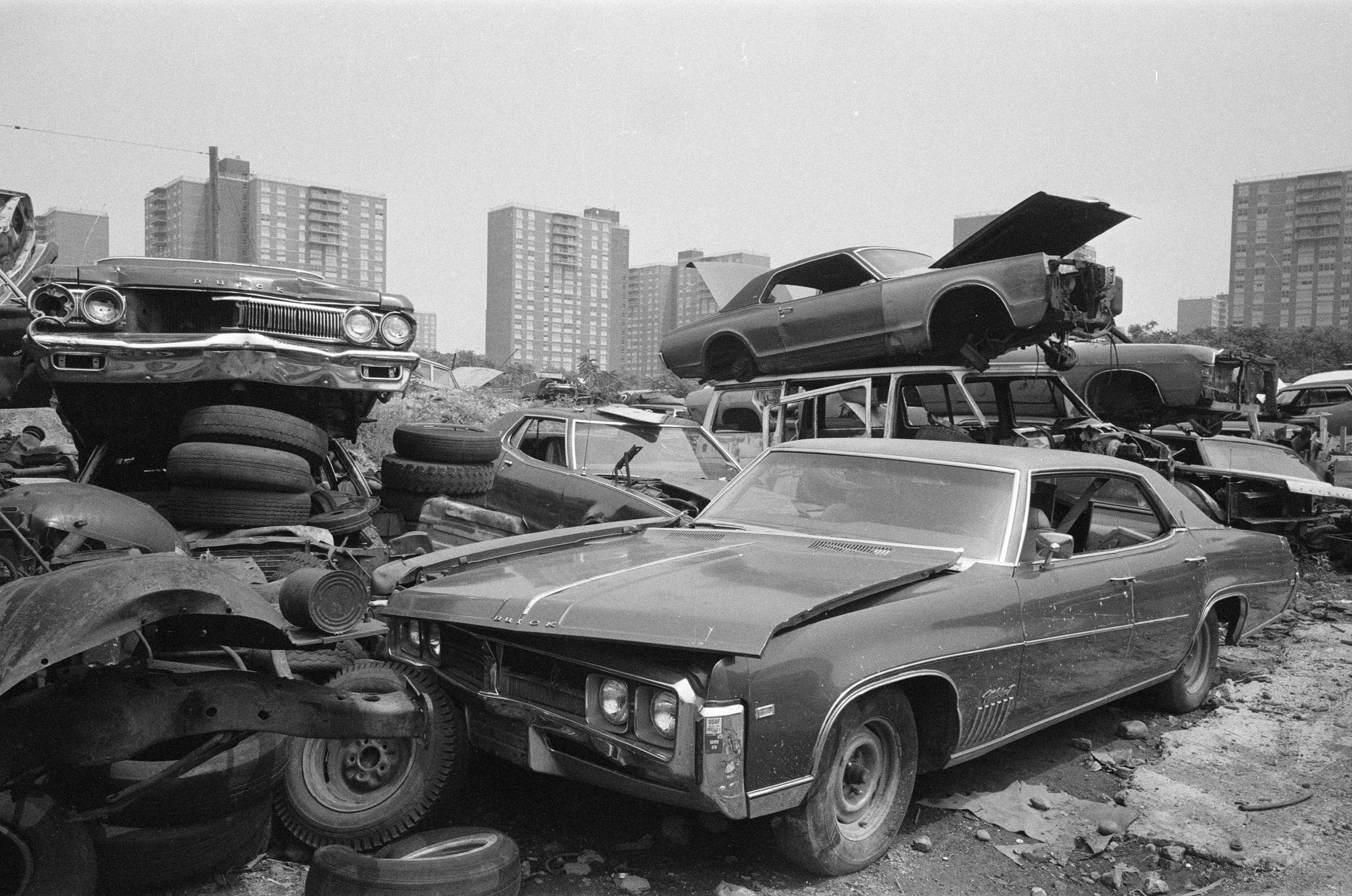 A black and white photo of broken down cars on scrap heap in New York.