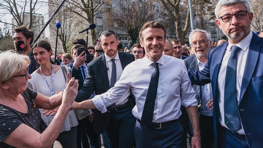 Emmanuel Macron stands among a crowd of people holding hands with a voter