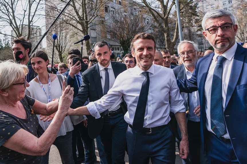 Emmanuel Macron stands among a crowd of people holding hands with a voter