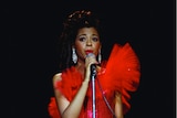 Singer Irene Cara performs wearing a red dress with a black background