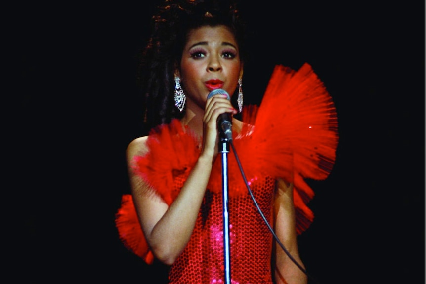 Singer Irene Cara performs wearing a red dress with a black background