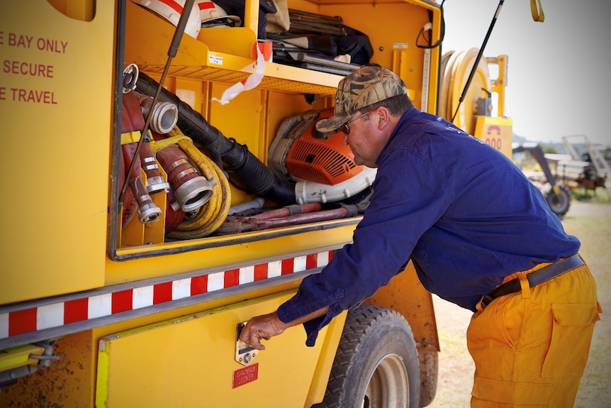 A photo of Anthony Sylvester wearing his fire brigade uniform and looking into a yellow fire truck.