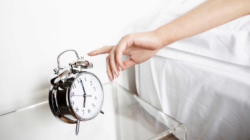 arm stretching out of bed to turn off alarm clock