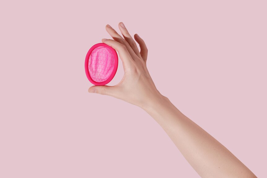 hand holding up a menstrual disc on pink background