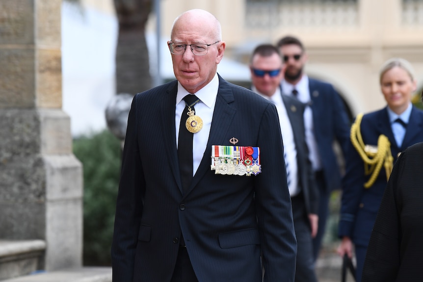 A bald man wearing a suit and military medals ribbon.