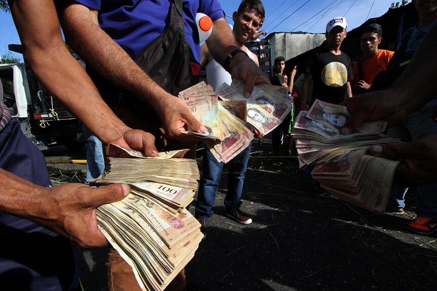 People hold up 100-Bolivar notes during a protest over lack of cash.