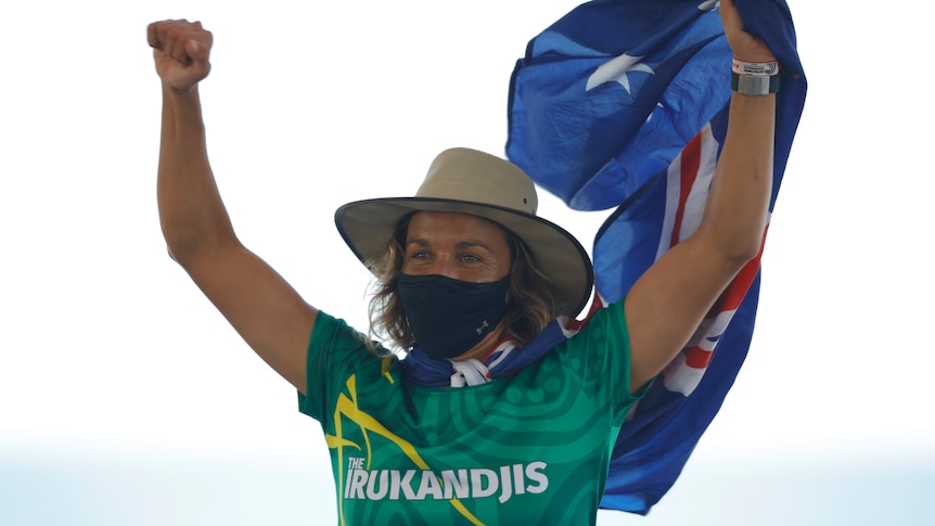 An Australian female surfer raises her arms on a podium as she celebrates winning gold at the World Surfing Games.