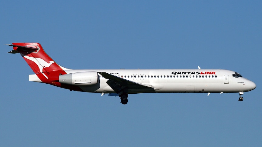 A QantasLink Boeng 717-200 plane flies on a blue sky backdrop 