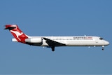 A QantasLink Boeng 717-200 plane flies on a blue sky backdrop 