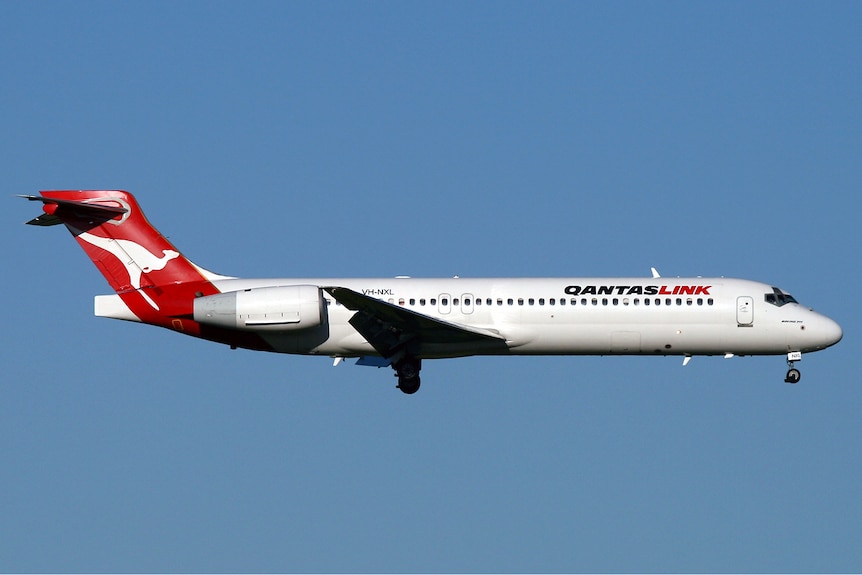 A QantasLink Boeng 717-200 plane flies on a blue sky backdrop 