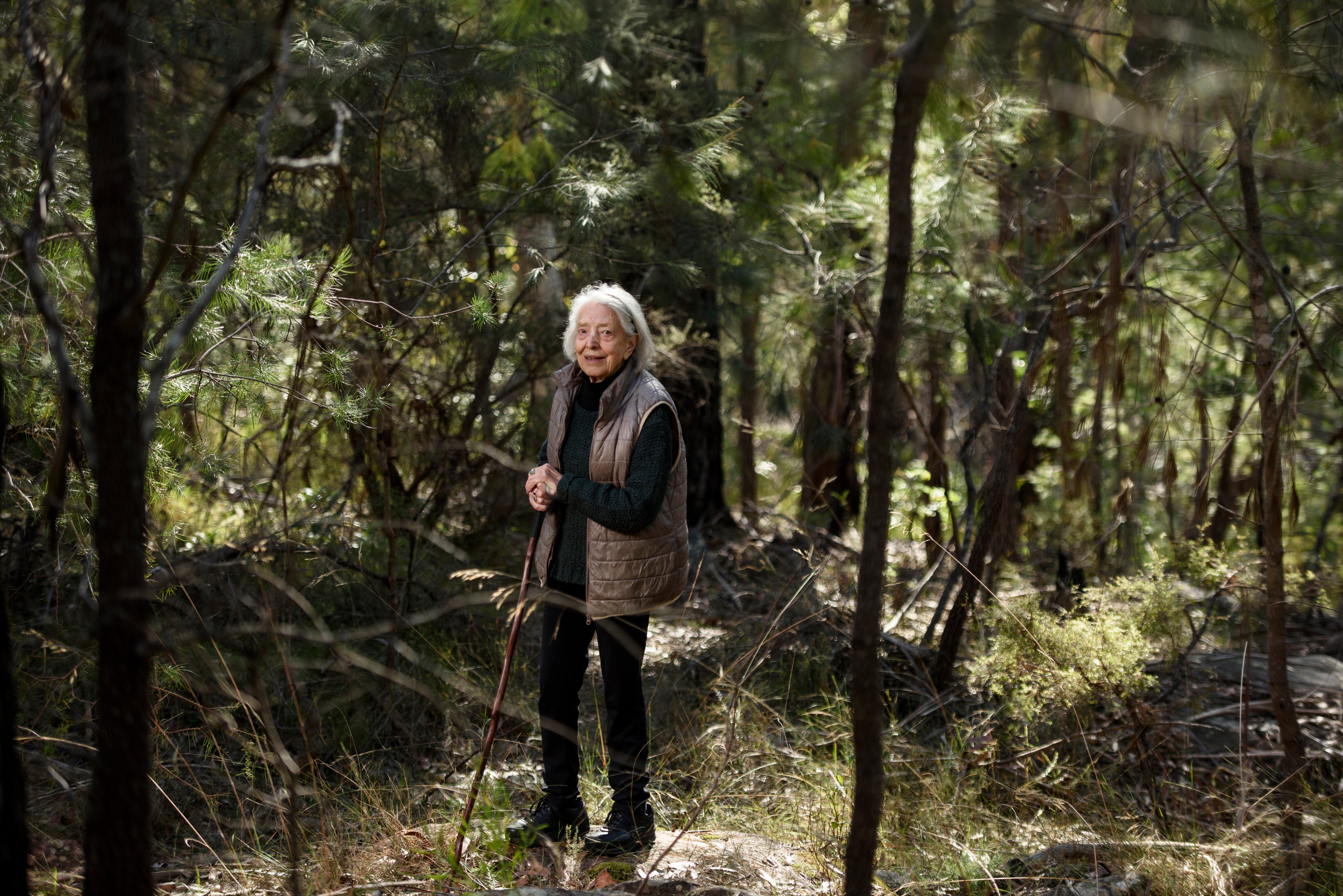A woman wearing a puffer jacket stands surrounded by bush.