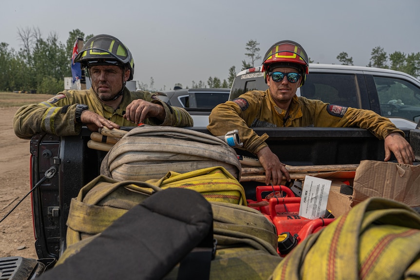 Two firefighters with ashened faces lean over the bed of a ute filled with firefighting hoses.