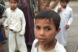 A group of kids in Yemen's Amran province pose for a photo. They are standing by a roadside, there is some grass but no trees.