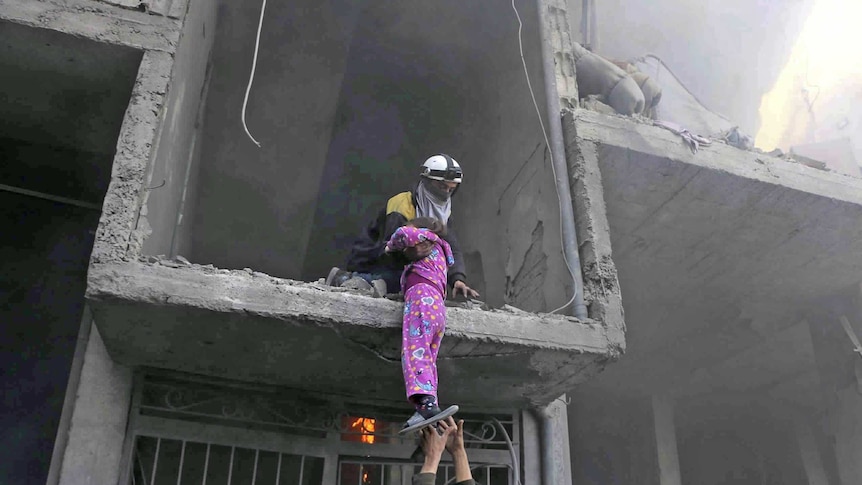 A member of the Syrian Civil Defence group rescues a young girl from a damaged building