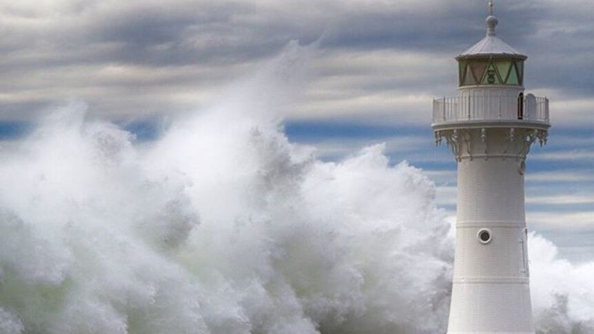 Waves crash against small white lighthouse