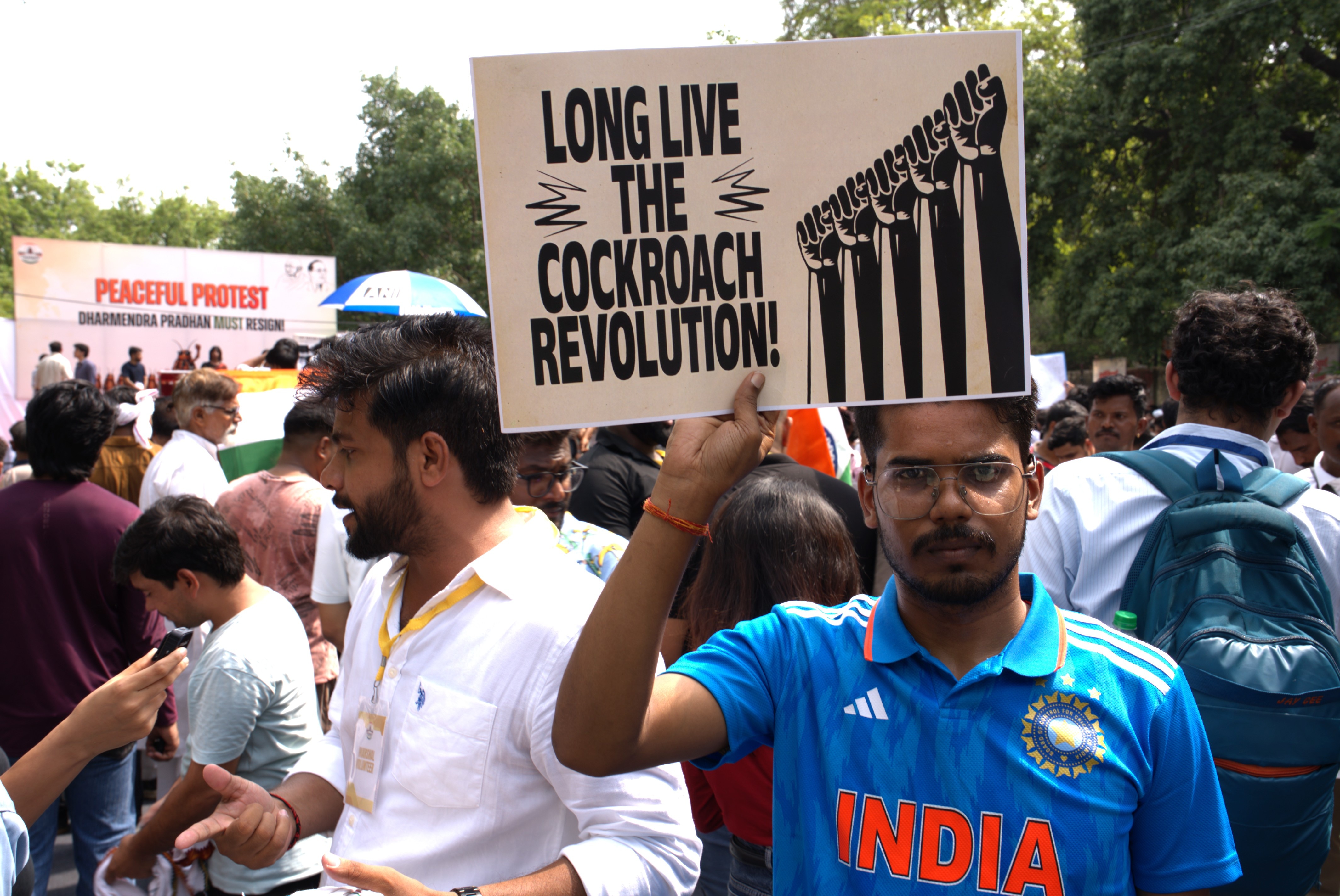 A man in a blue India sports shirt holds a sign that says "LONG LIVE THE COCKROACH REVOLUTION".