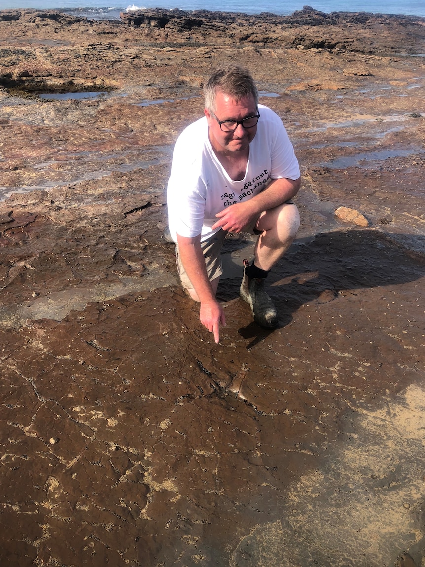 A man crouched on a marine rock platform