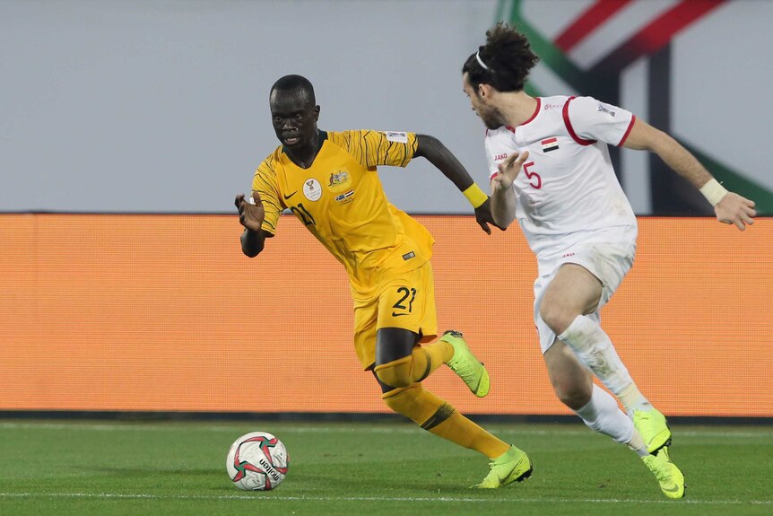 Socceroos' Awer Mabil runs alongside Syria's Omro Midani with a football at his feet during the Asian Cup.