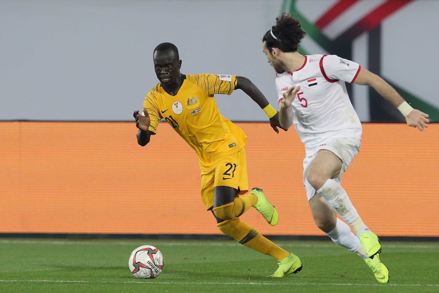 Socceroos' Awer Mabil runs alongside Syria's Omro Midani with a football at his feet during the Asian Cup.