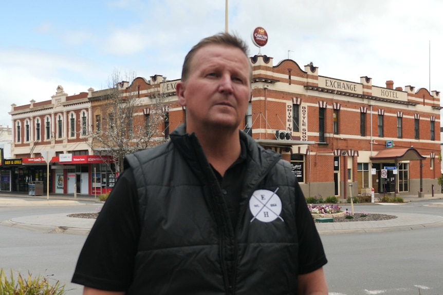 A man in a black vest standing in front of a pub