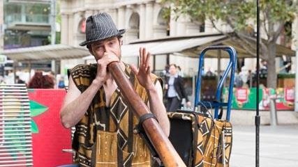 A busker plays the didgeridoo into a microphone on a Melbourne street.