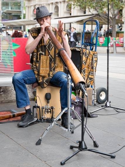 A busker plays the didgeridoo into a microphone on a Melbourne street.