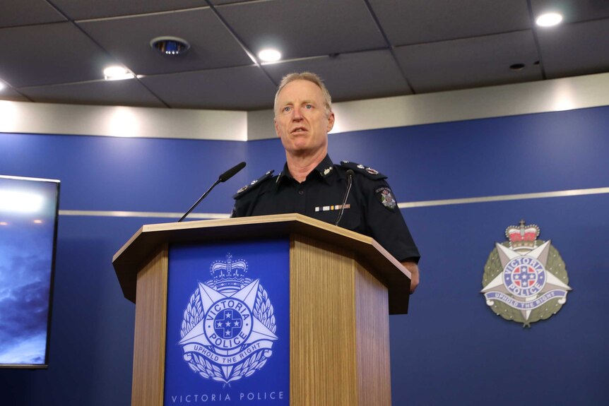 Deputy Commissioner Rick Nugent stands at a wooden lectern with the Victoria Police logo on the front.