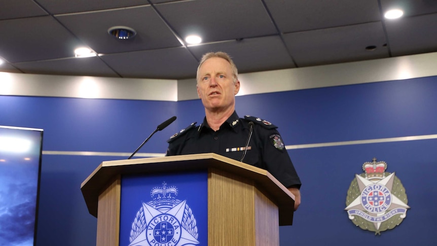 Deputy Commissioner Rick Nugent stands at a wooden lectern with the Victoria Police logo on the front.