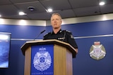 Deputy Commissioner Rick Nugent stands at a wooden lectern with the Victoria Police logo on the front.