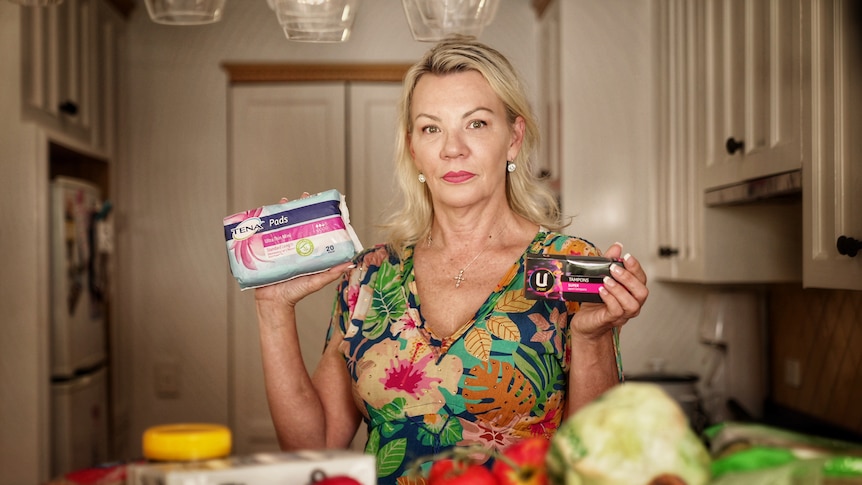 A woman holding up sanitary products in her kitchen
