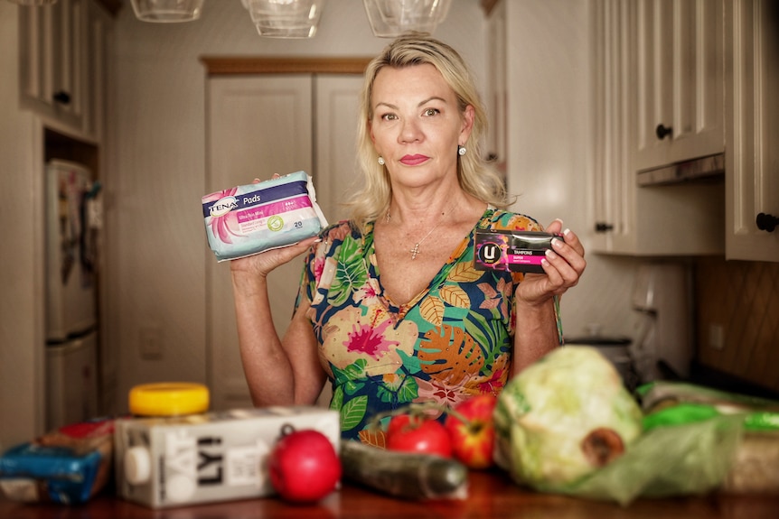 A woman holding up sanitary products in her kitchen