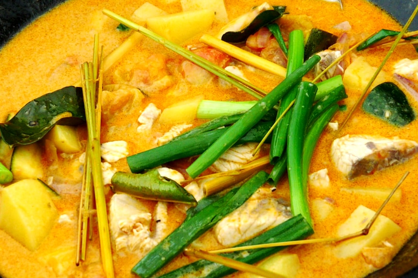 Close-up on a yellow-orange coloured curry featuring chunks of fish and greens.