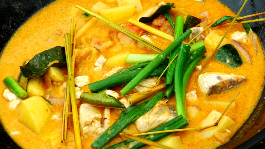 Close-up on a yellow-orange coloured curry featuring chunks of fish and greens.