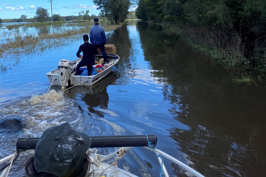 Two men in a boat navigating the floodwaters, while another follows.