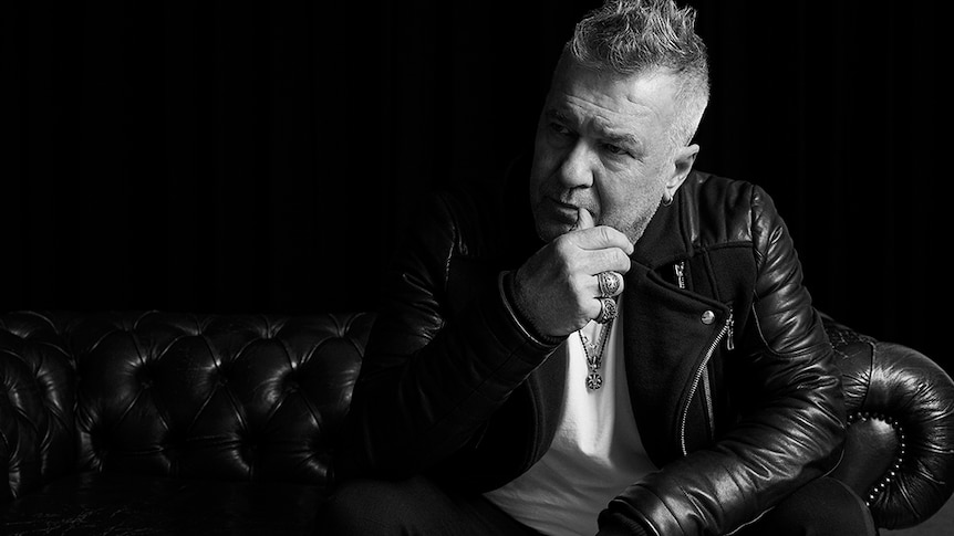 Rock singer Jimmy Barnes sitting on a leather couch looking pensive