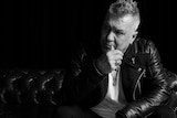 Rock singer Jimmy Barnes sitting on a leather couch looking pensive