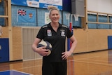 woman in black shirt holding ball stand smiling with hand on hip on basketball court
