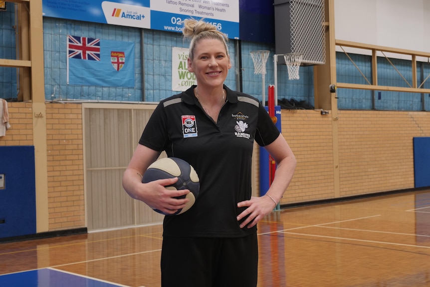 woman in black shirt holding ball stand smiling with hand on hip on basketball court