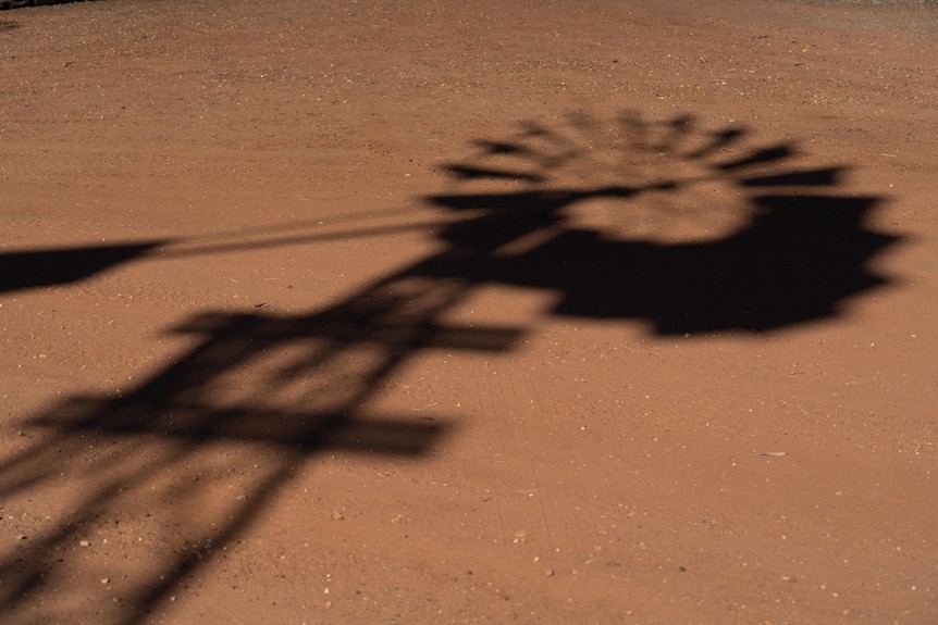 The shadow of a windmill falls across red dirt.