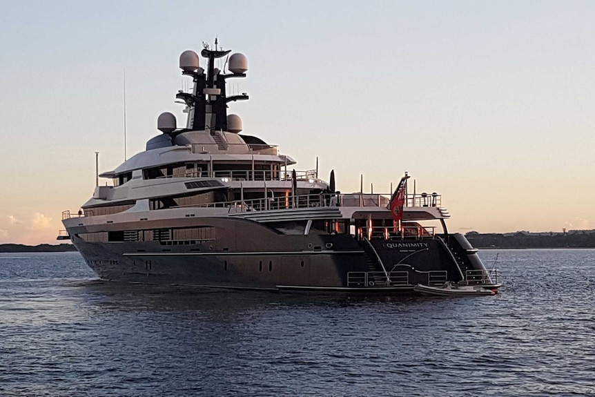 Rear angle view of the Equanimity super yacht on a calm sea at twilight with land in the distance