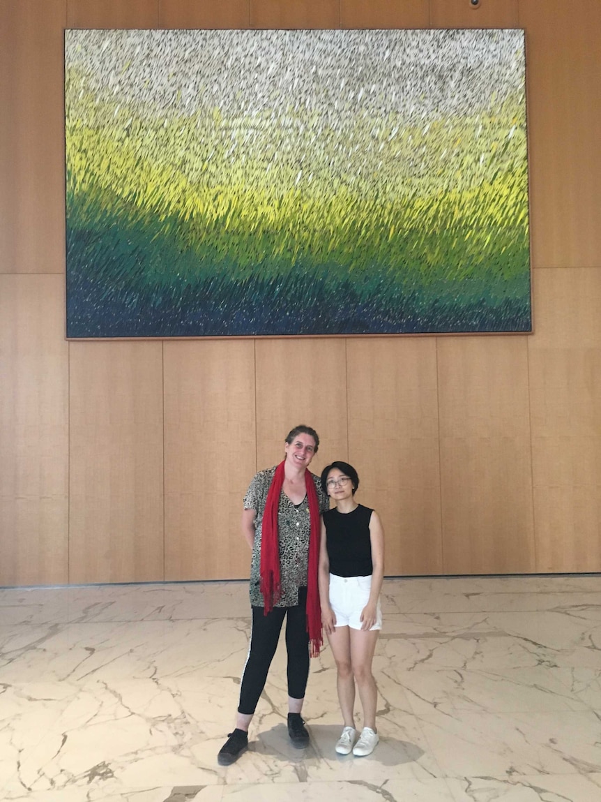 Two women stand in front of large art work