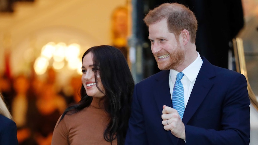 Prince Harry and Meghan, Duchess of Sussex leave a building. Both are smiling excitedly.