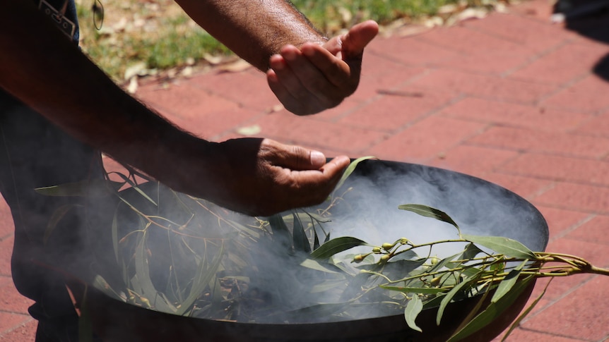 A pair of hands handling eucalyptus at a smoking ceremony